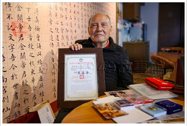 圖三 吳志輝先生手持「八二三」砲戰參戰證書，桌面上擺放著獲得的諸多獎章。